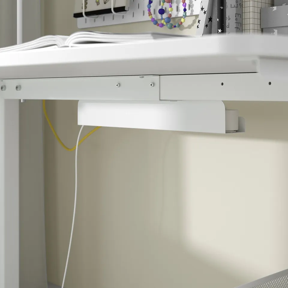 Underneath white desk with cable management, yellow and white cords visible. Desk has clean, minimalist design.