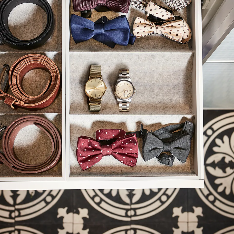 White wardrobe drawer with felt organisers: watches, bow ties, belts, sweater.