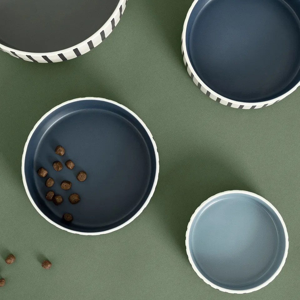 Four stoneware pet bowls of varying sizes on green surface. One bowl contains dog food, showing its practical use.