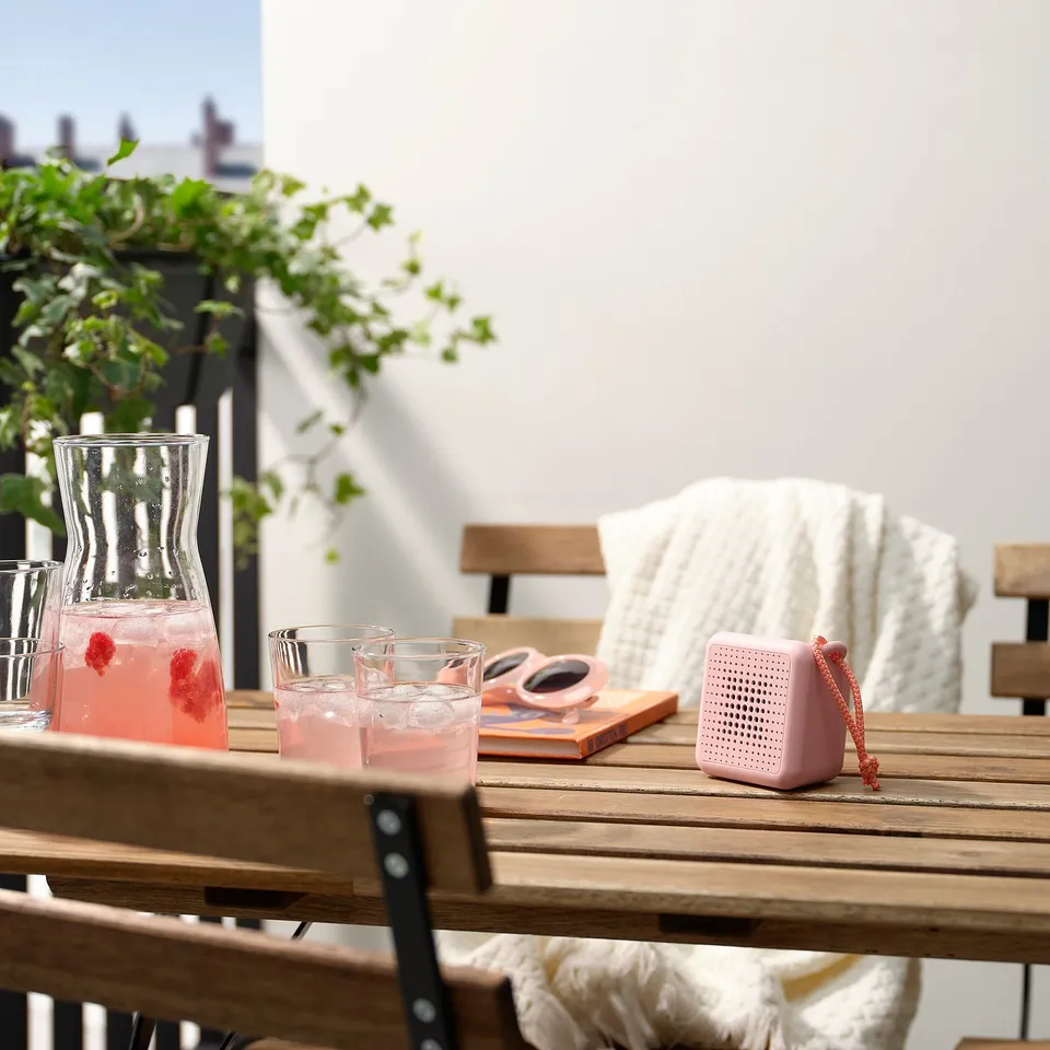Patio with lemonade, glasses, pink speaker & book. Waterproof, bluetooth speaker for outdoor use.