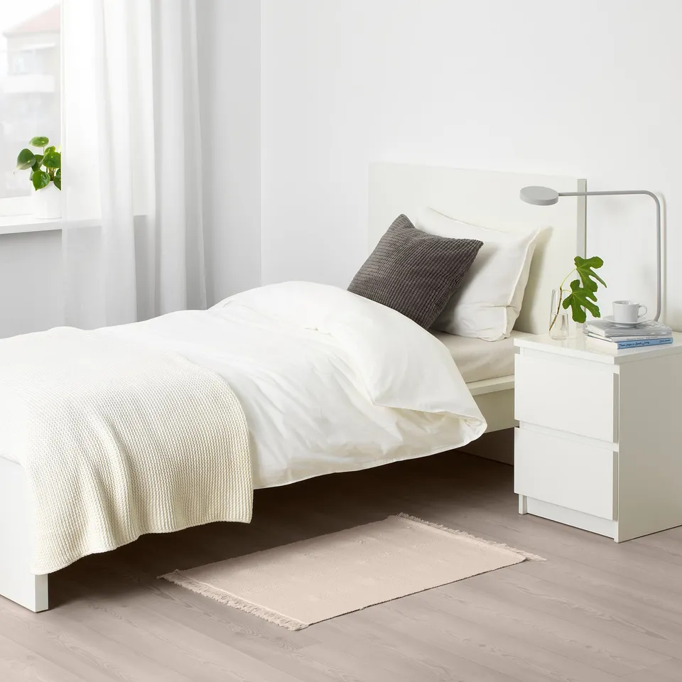 Minimalist bedroom with white SORTSÖ rug, bedside table, and lamp.
