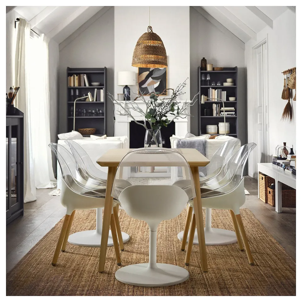 Modern dining table with four BALTSAR chairs, white, clear seats, wooden legs, and a vase with branches.