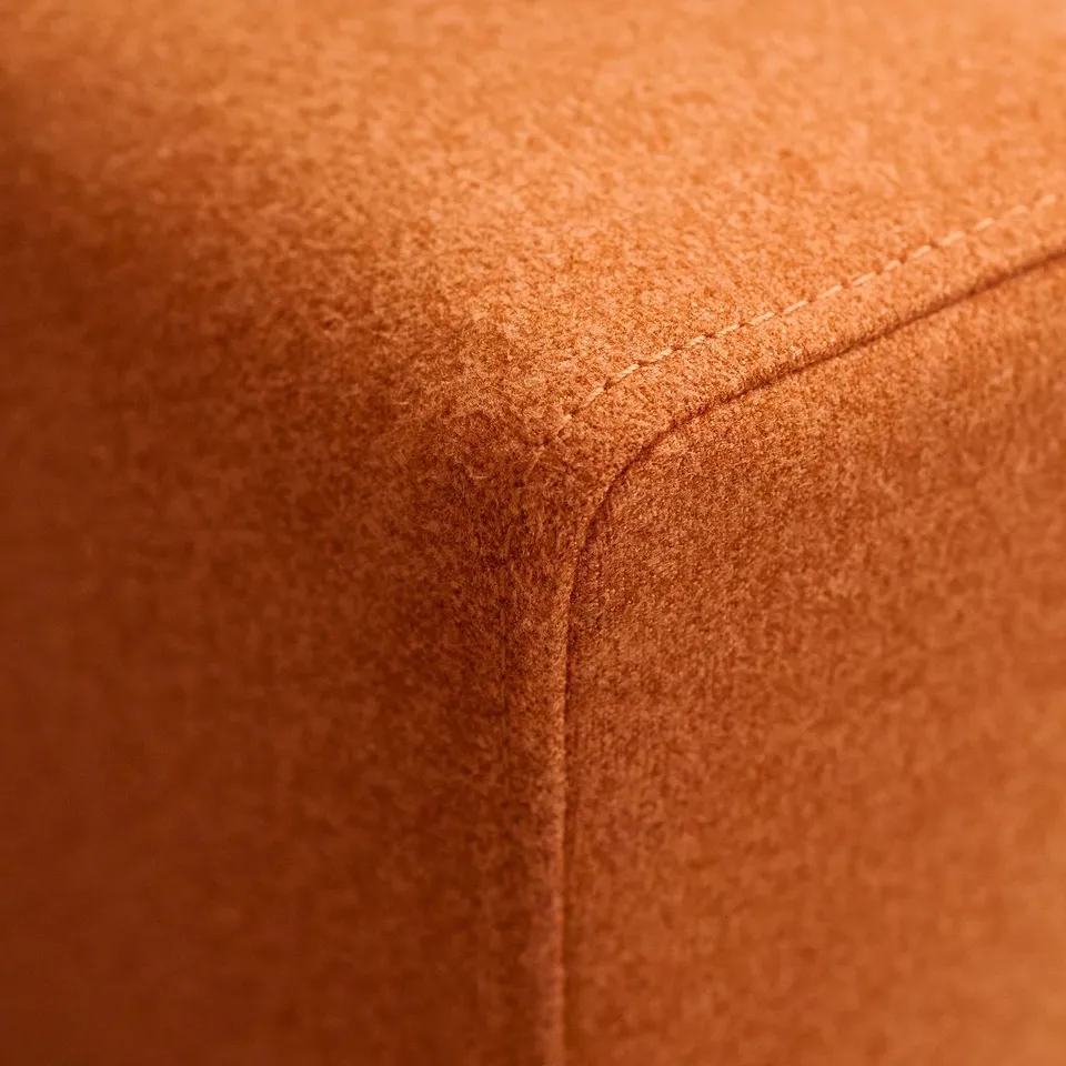 Close-up of a plush, orange footstool with neat stitching detail. Soft texture and high-quality fabric evident.