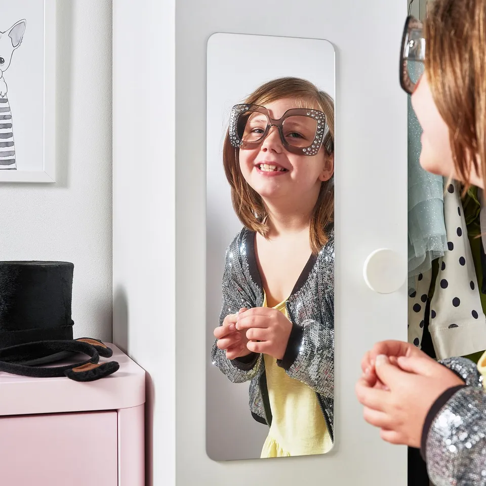 A child uses a mirror on a wardrobe door to check their outfit and hair before leaving.