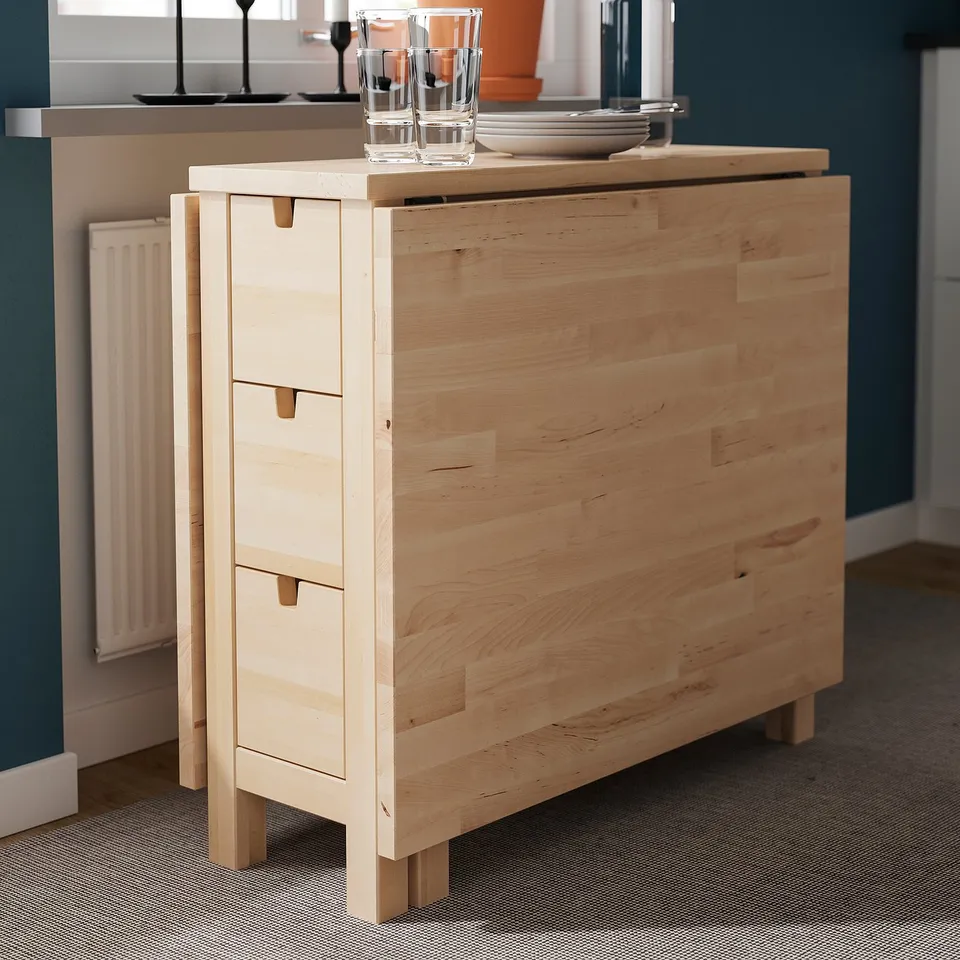 Light wood folding table with drawers, displaying glasses and plates.