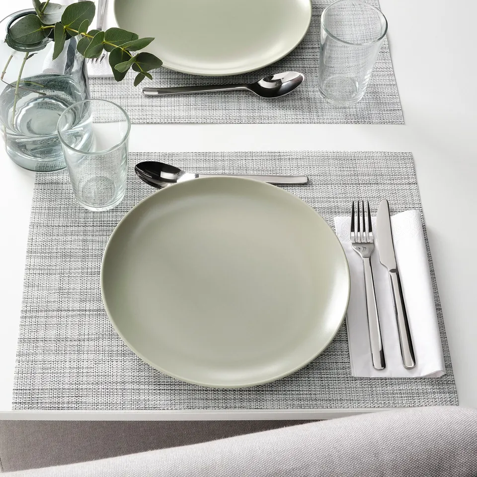 Two table settings with plates, forks, knives, spoons, glasses, and plants on woven placemats.