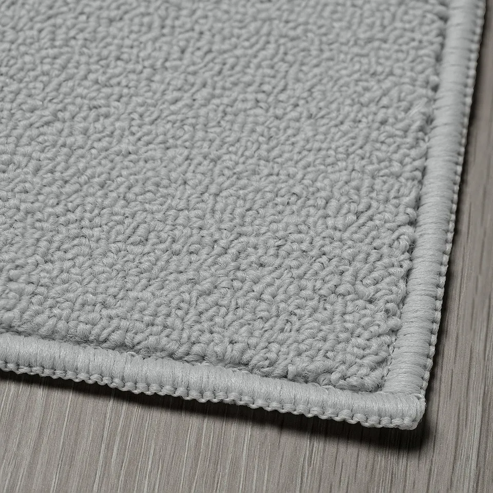 Close-up of textured grey kitchen mat on wooden floor, showcasing its soft, quality material and secure stitching.