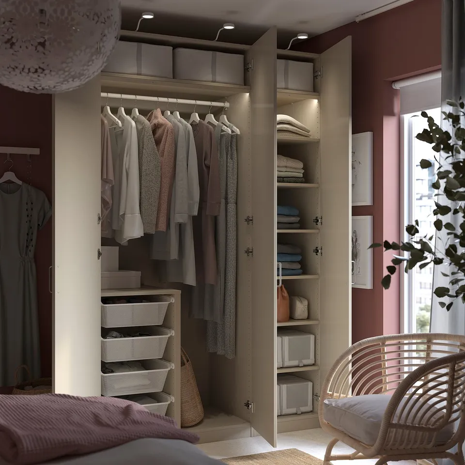 A modern closet with beige PAX wardrobes has clothes, shelves, and baskets with soft-close hinges and integrated lighting.
