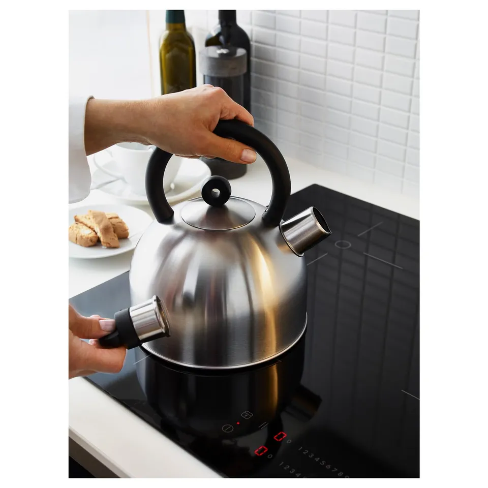 Hand lifts whistling VATTENTÄT kettle from modern hob after boiling water. Sleek design handles prominently featured.