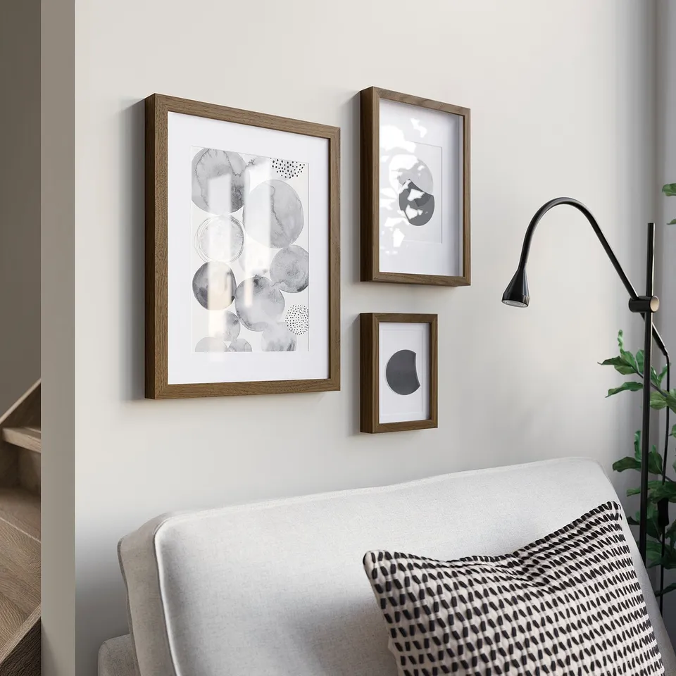 Three RÖDALM frames above sofa. Largest left, medium centre, small right. Modern abstract art. Black lamp, plant far right.