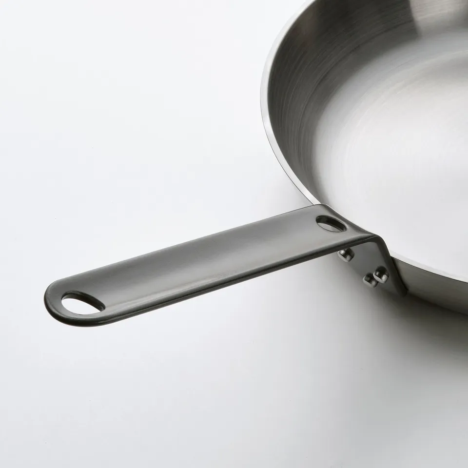 Close-up of a high-quality carbon steel frying pans handle, reflecting light, indicating its durability and sleek design.
