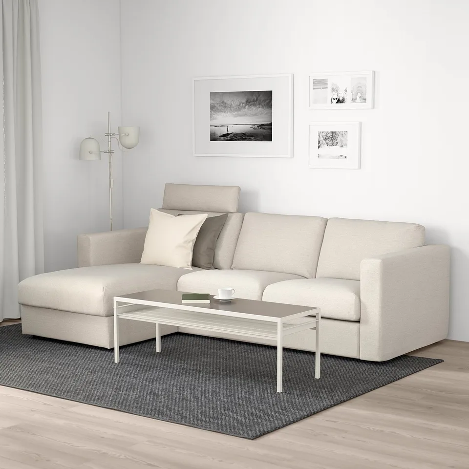 Modern minimalist living room: beige VIMLE sofa with chaise, white coffee table, black patterned rug, wall art, sleek floor lamp.