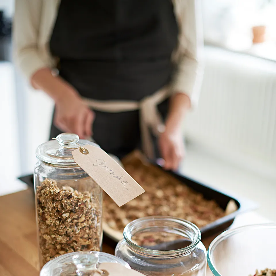 Person preparing food with VARDAGEN granola and muesli jars on counter.