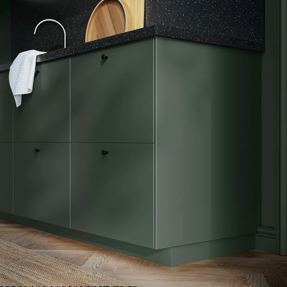 Kitchen cabinets with HAVSTORP dark green smooth fronts, black countertop, white sink, wooden floor, white towel.