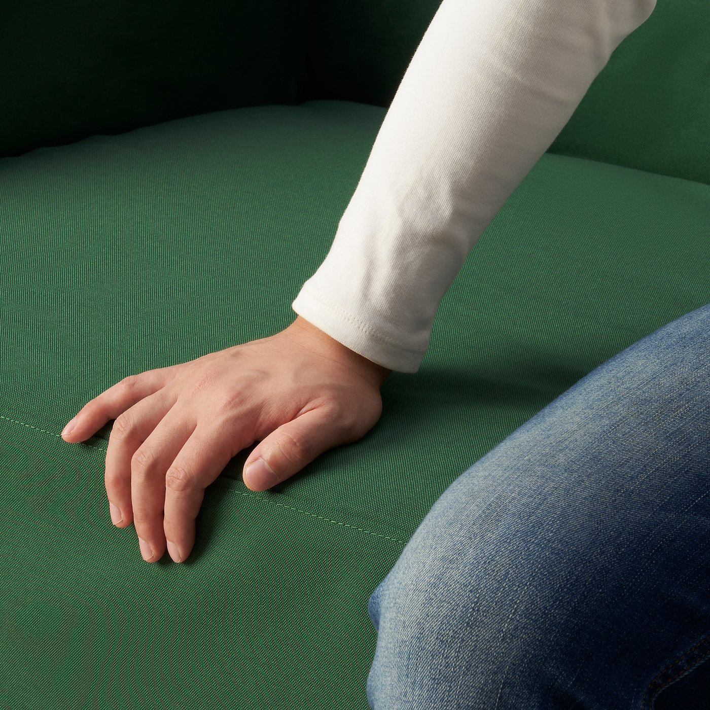 Hand on green sofa, white sleeve and jeans.