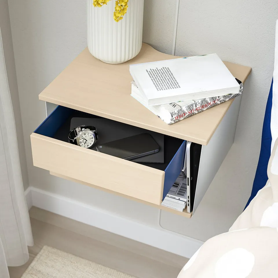 Modern wall-mounted bedside table with open storage for books and a drawer for personal items, featuring cable cut-outs for convenience.