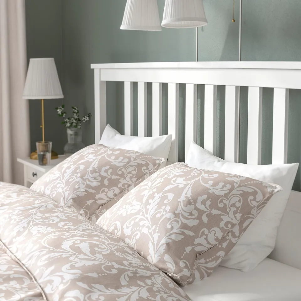 A cosy bed with ornate patterned pillows and a sturdy white headboard, part of the HEMNES series from IKEA.