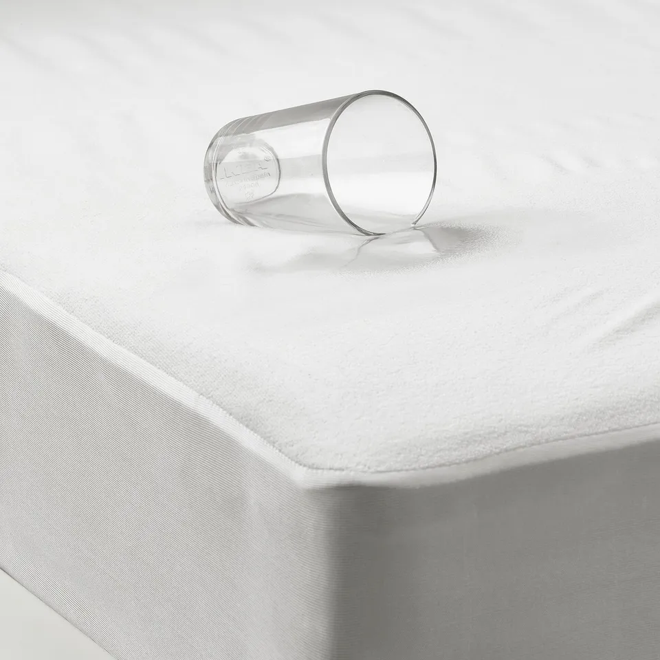 A thin, waterproof mattress protector shown on top of a mattress. A glass with water is placed on it, demonstrating its liquid-resistant function.