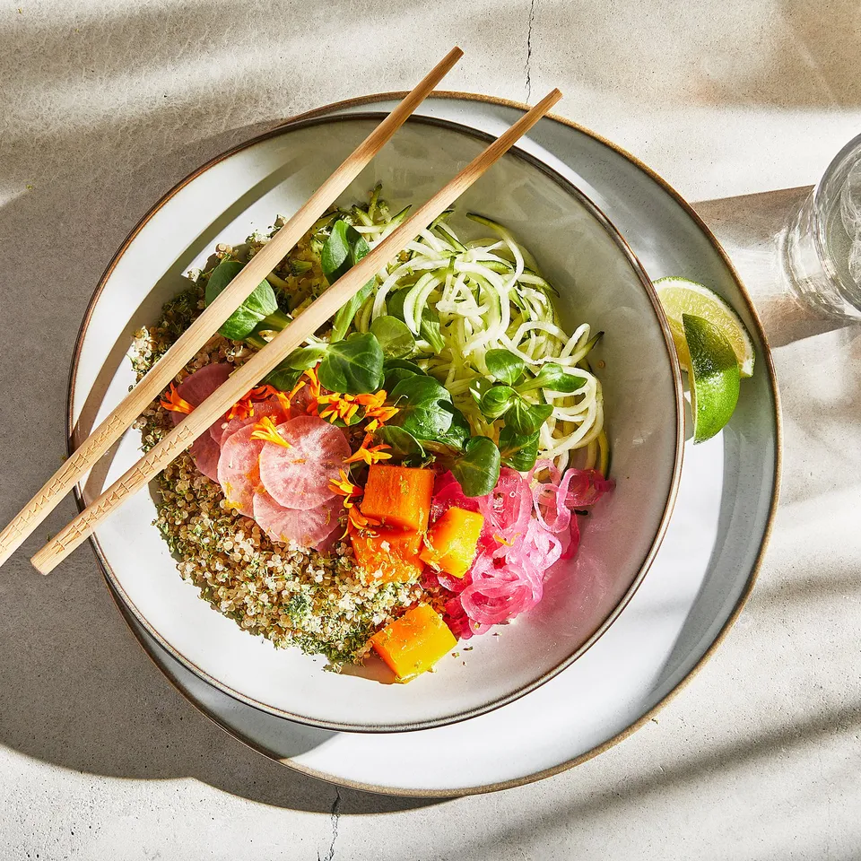 A bowl with quinoa, vegetables, and chopsticks. Chopsticks are placed across the bowl.