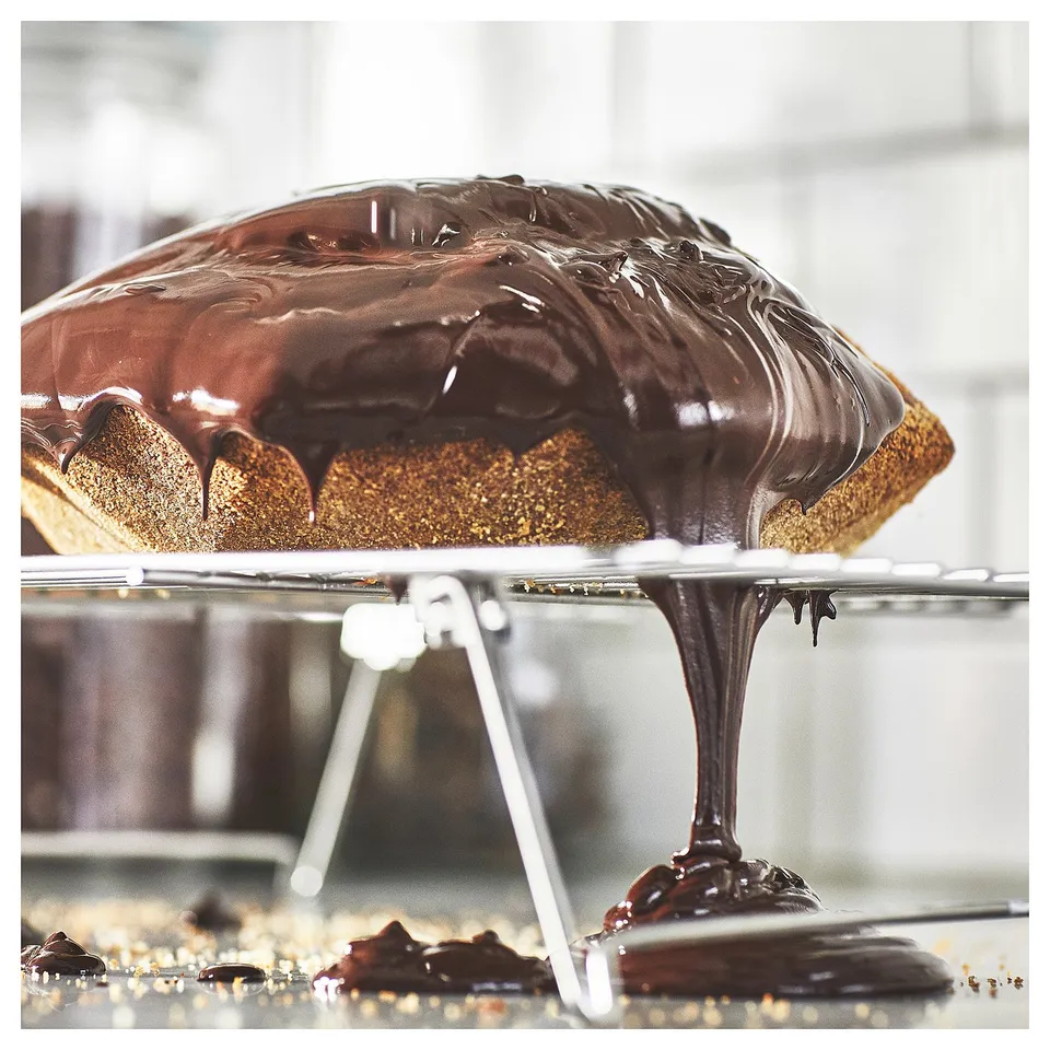 Dark chocolate-drizzled dessert on clear stand. Rich, glossy finish. Stainless steel legs.
