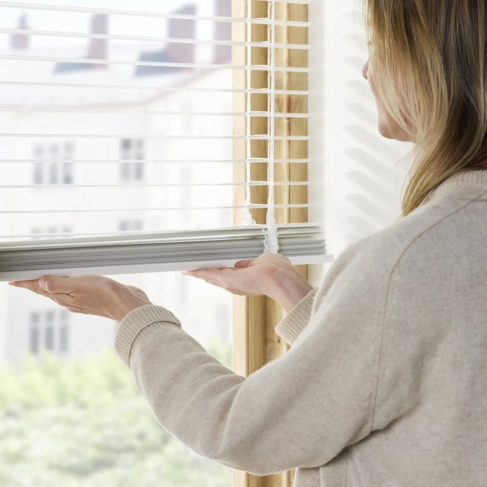 A person adjusts venetian blinds by pulling a cord, controlling light and privacy.