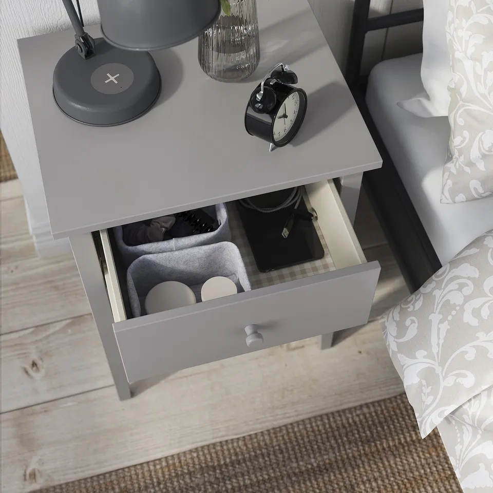 Bedside table with lamp, clock, and vase; drawer with sunglasses and bags.