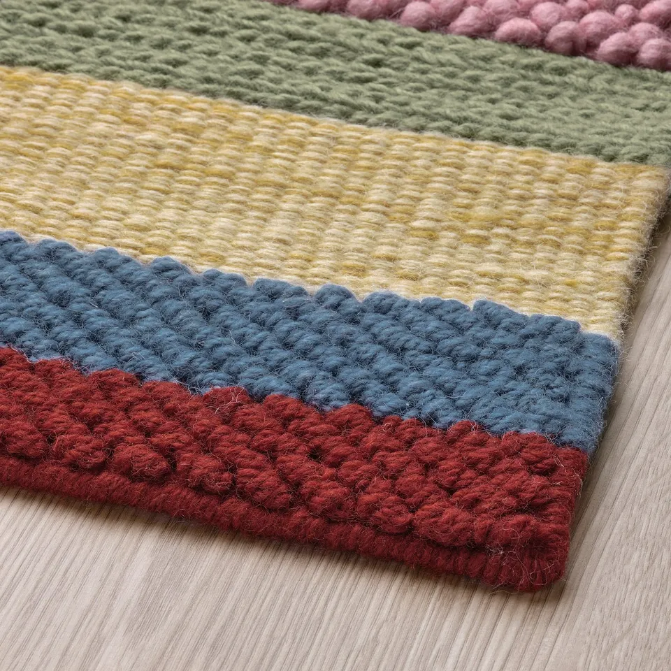 Handwoven colourful wool rug with distinct stripes and textures on wooden floor.