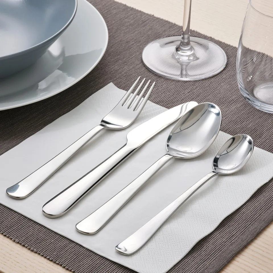 Table setting with fork, knife, and spoons on grey napkin, plate, and glass.