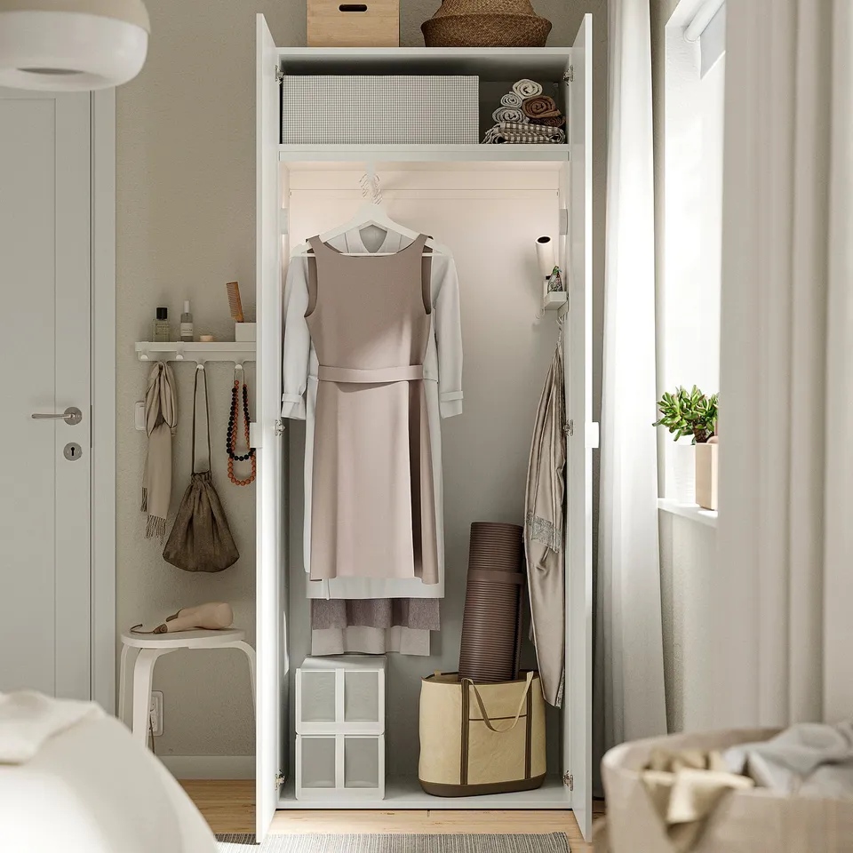 Open wardrobe displaying organised clothing and storage: dresses hung, folded clothes, bins, and shelves with items.