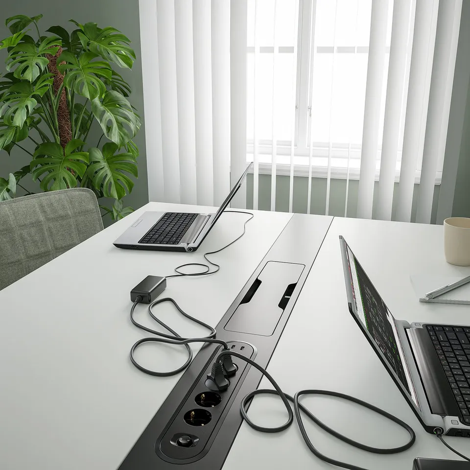 Modern desk with power outlets, laptops, and plants.