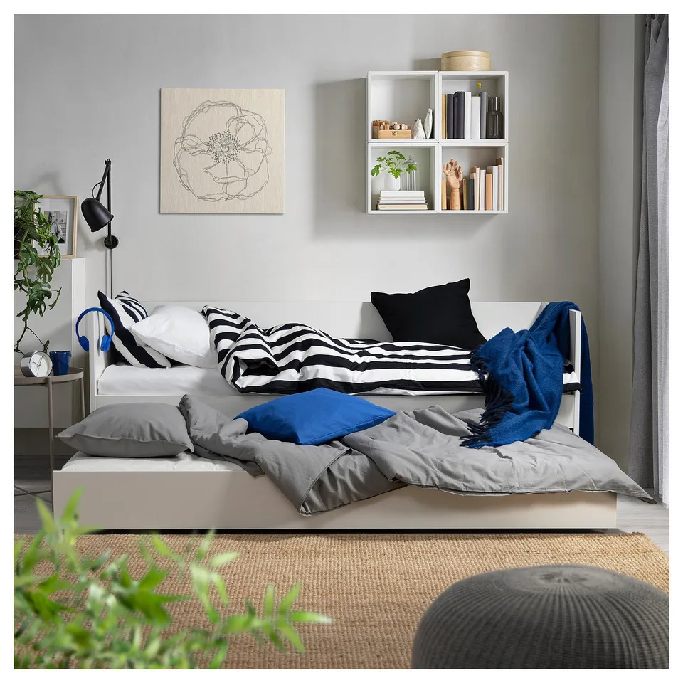 Cosy bedroom with a white and blue daybed. Striped pillows, grey blanket, grey wall, and a simple canvas print.