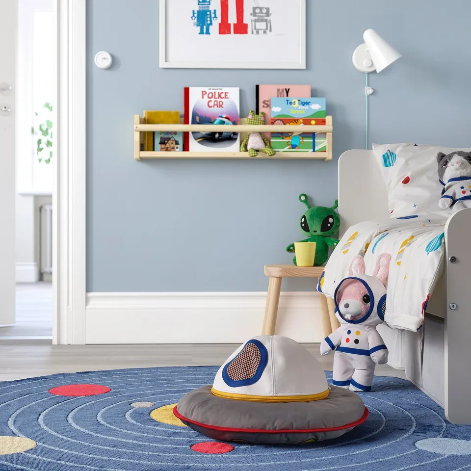 Childs space-themed room with blue walls, bed, astronaut toy, & themed decor.