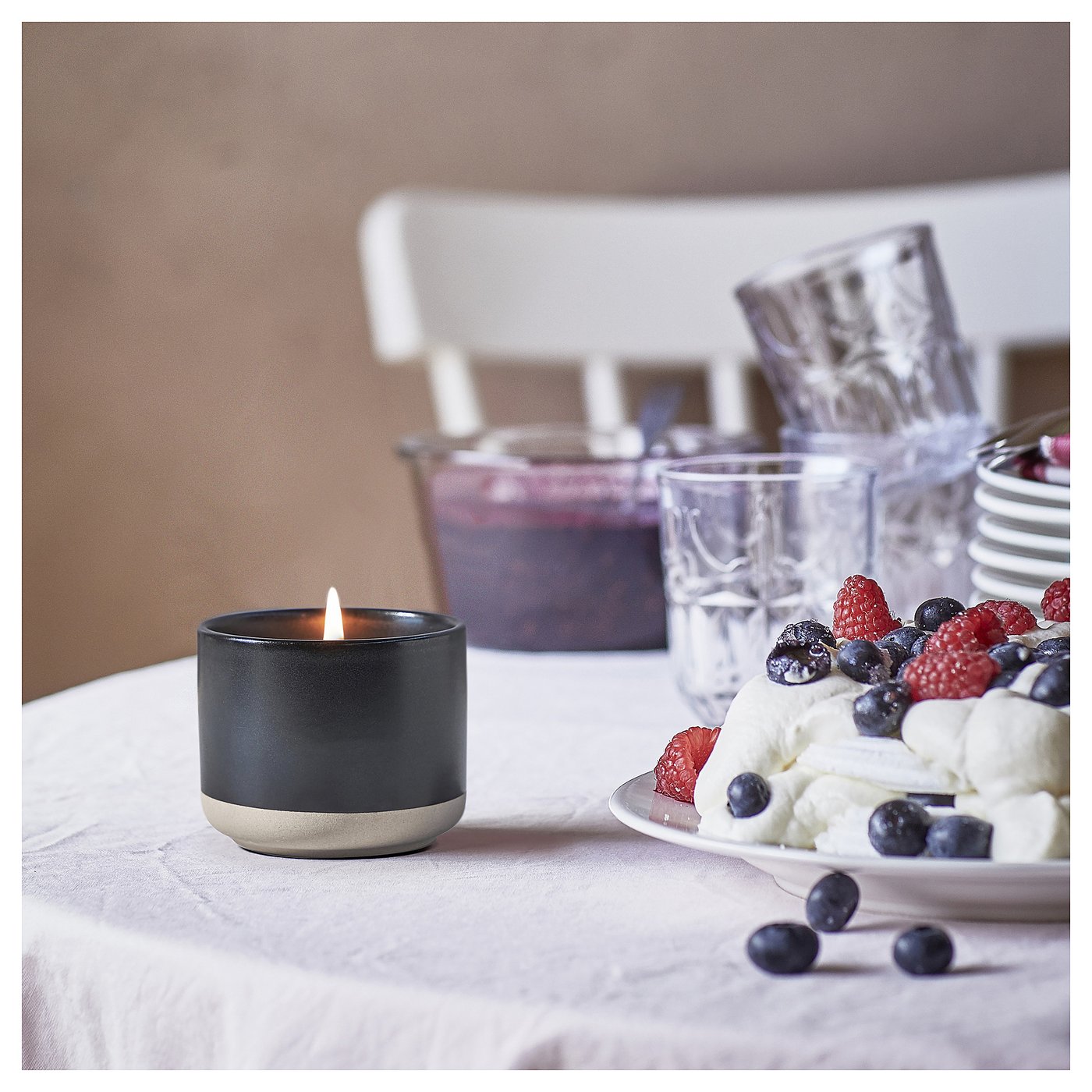 A lit black STÖRTSKÖN candle sits beside a plate of berries, cream, and glasses on a dining table.