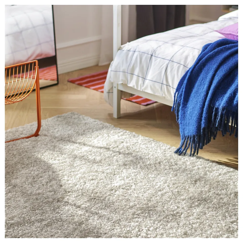 Grey ÄRENDE rug in bedroom, blue blanket on white bed adds cosiness.