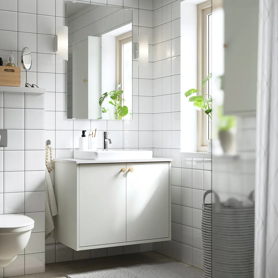 Modern white bathroom with HAVBÄCK vanity, mirror, semi-recessed sink, towel rack, and striped laundry basket.