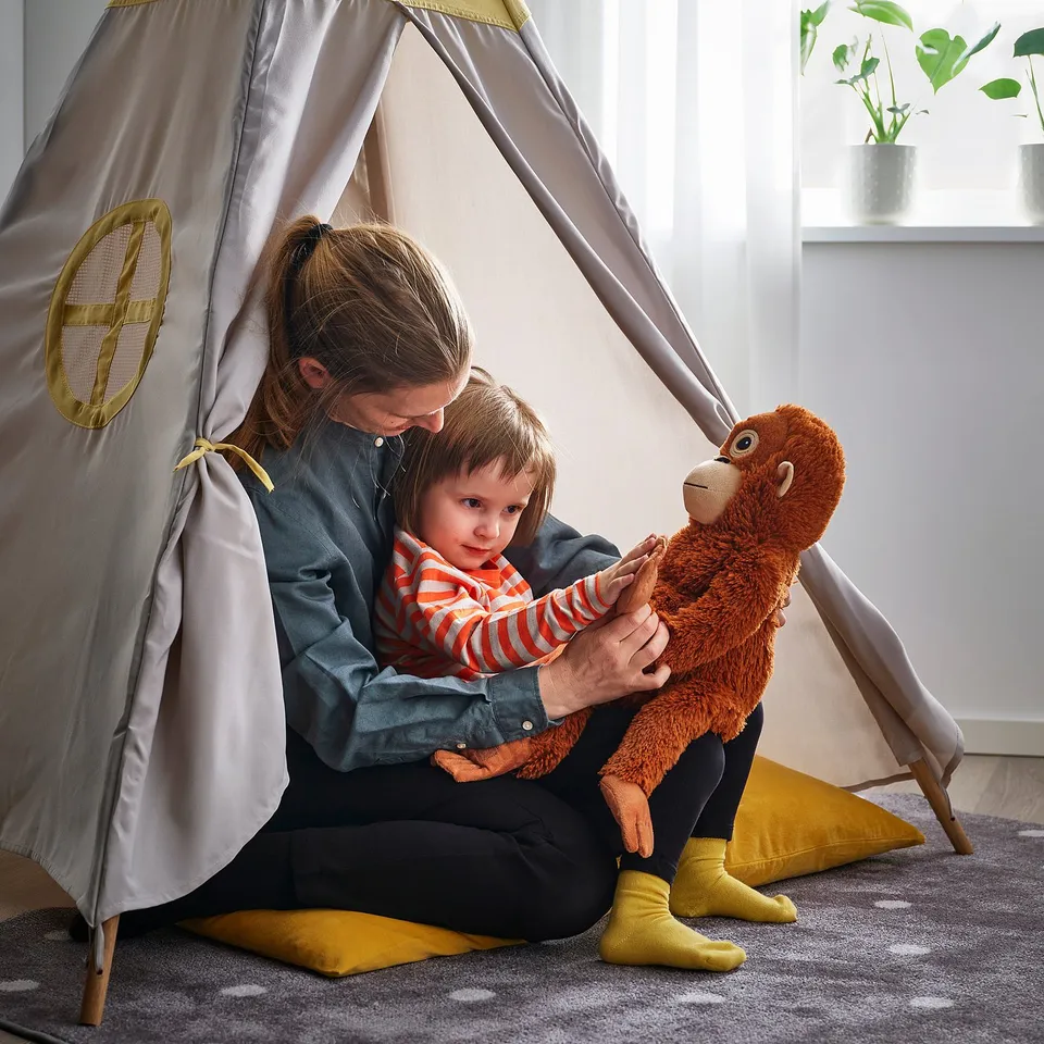Adult and child playing with soft toy monkey in cosy tent.