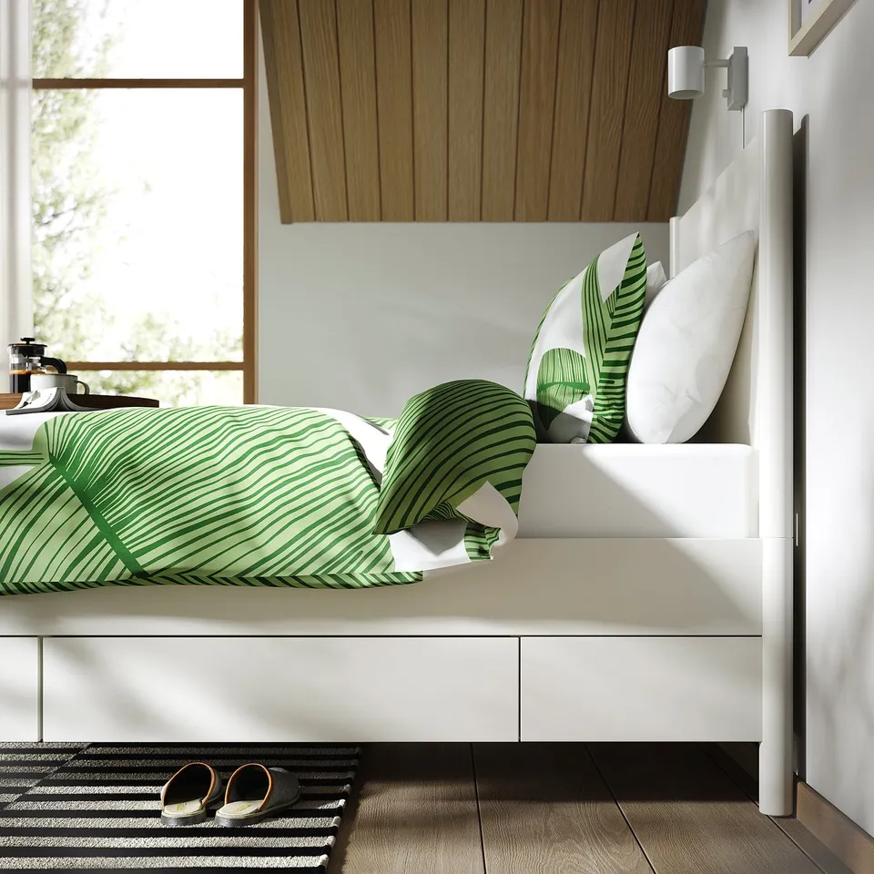 Bed with soft-close drawers, green palm leaf bedding, slatted base, natural wood accents, bright lighting, cosy setting.