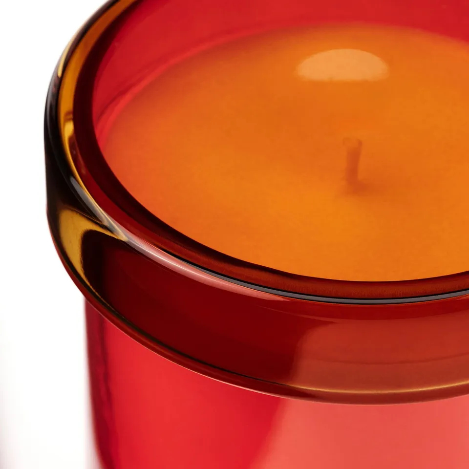 Close-up of vibrant red candle with orange wax, lit wick, smooth edges, and reflective surface.