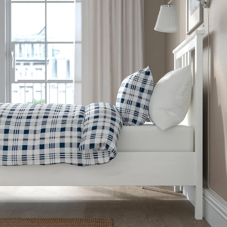 Plaid bedding on white wooden bed by window.