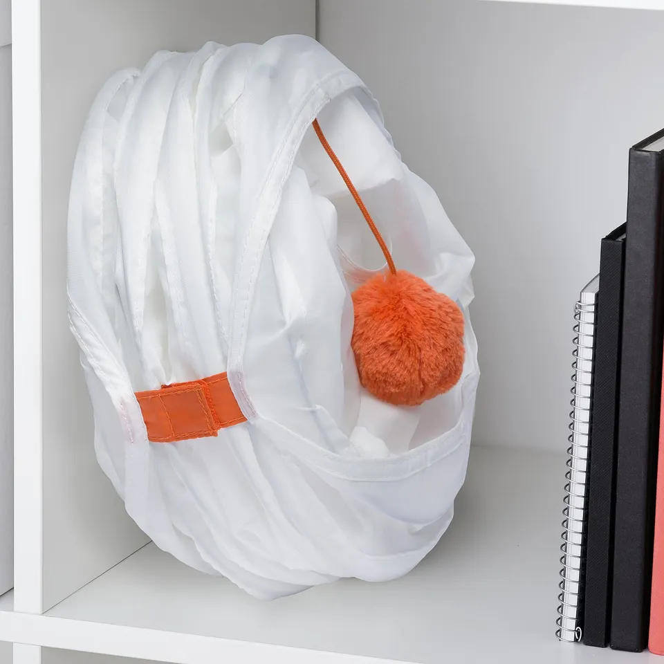 White cat play tunnel with orange pom-pom and handle on shelf.