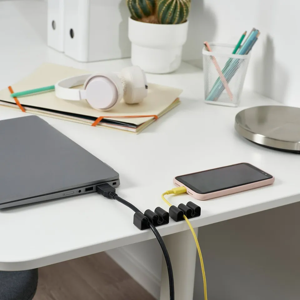 A clean desk setup with a laptop, smartphone charging, and organised with KALKSTUFF cable holders keeping cords tidy.