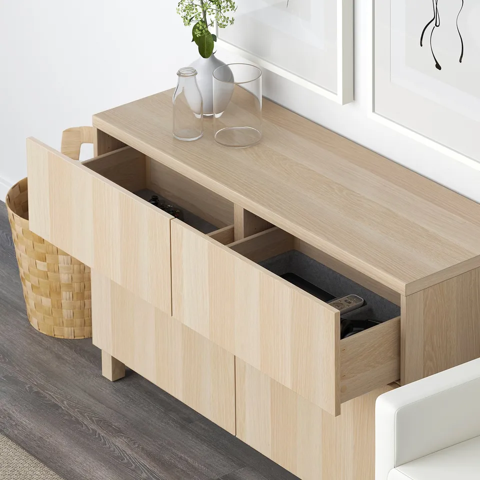 Light wood sideboard with open drawers, storing remote and other items. Top decorated with vases.