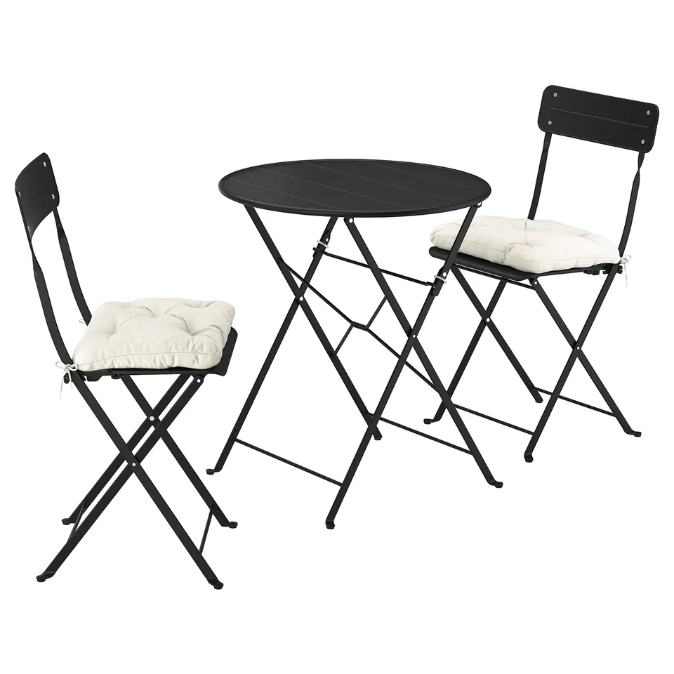 Black metal outdoor bistro set with round table and two chairs, each having a beige cushion. Compact and foldable design.