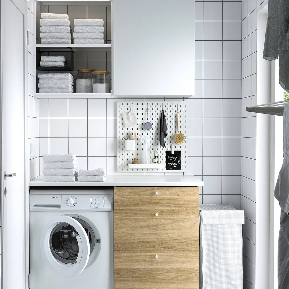 Small, white SKÅDIS pegboard beside washing machine in laundry, displays towels.