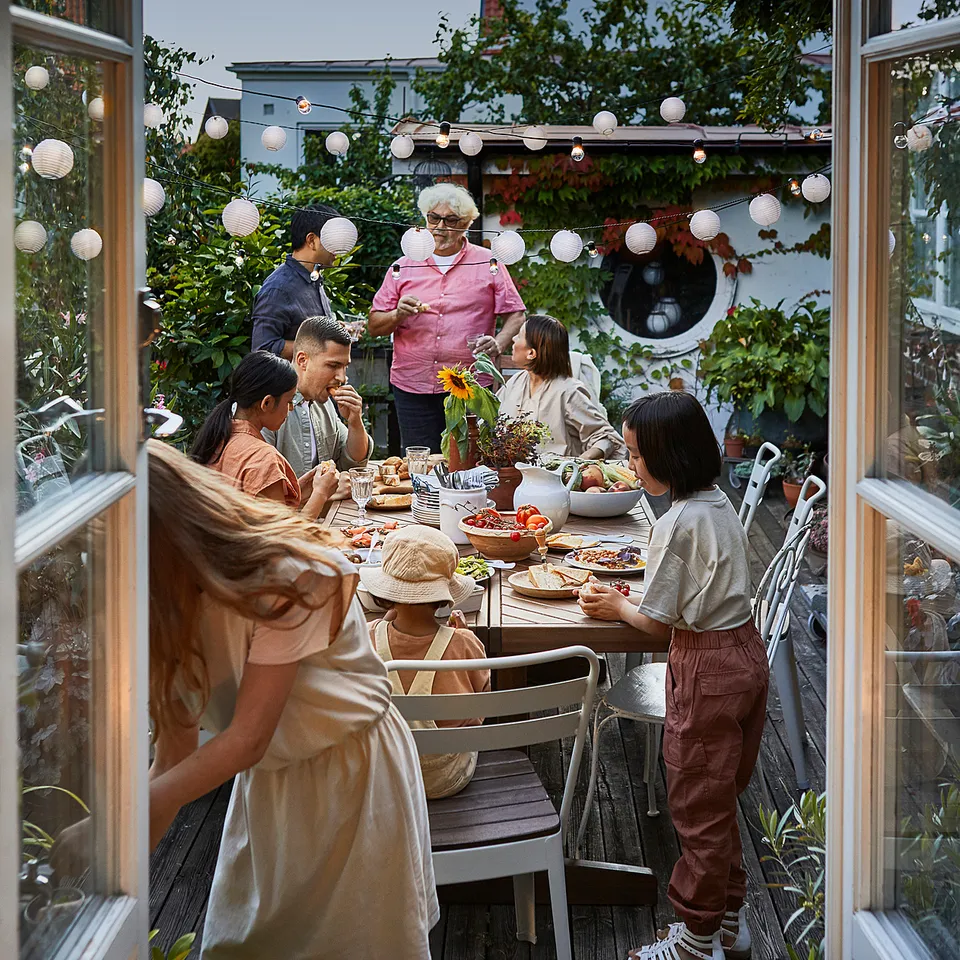 Family enjoying meal at farmhouse NORRMANSÖ table with paper lanterns and greenery.
