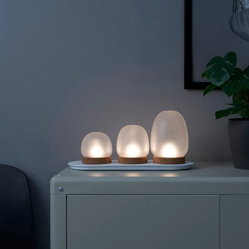 Three small table lamps on a white tray, emitting warm, flickering light, positioned on a blue surface.