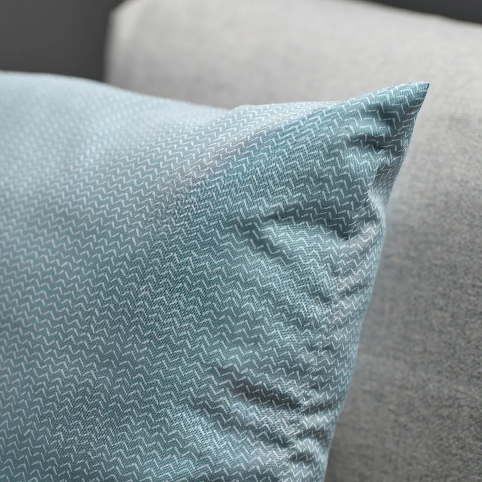 Teal geometric throw pillow, with intricate zigzag pattern, sits on a stylish neutral sofa.