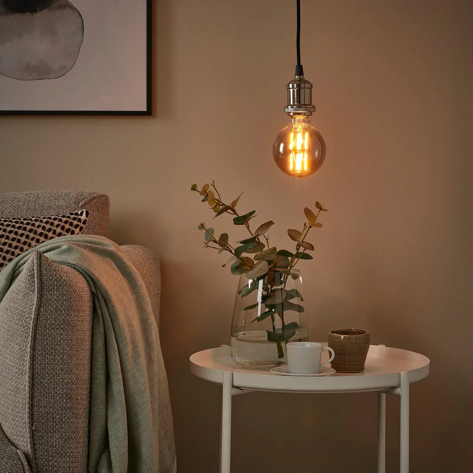 Cosy corner with MOLNART led bulb, side table, blanket, painting.