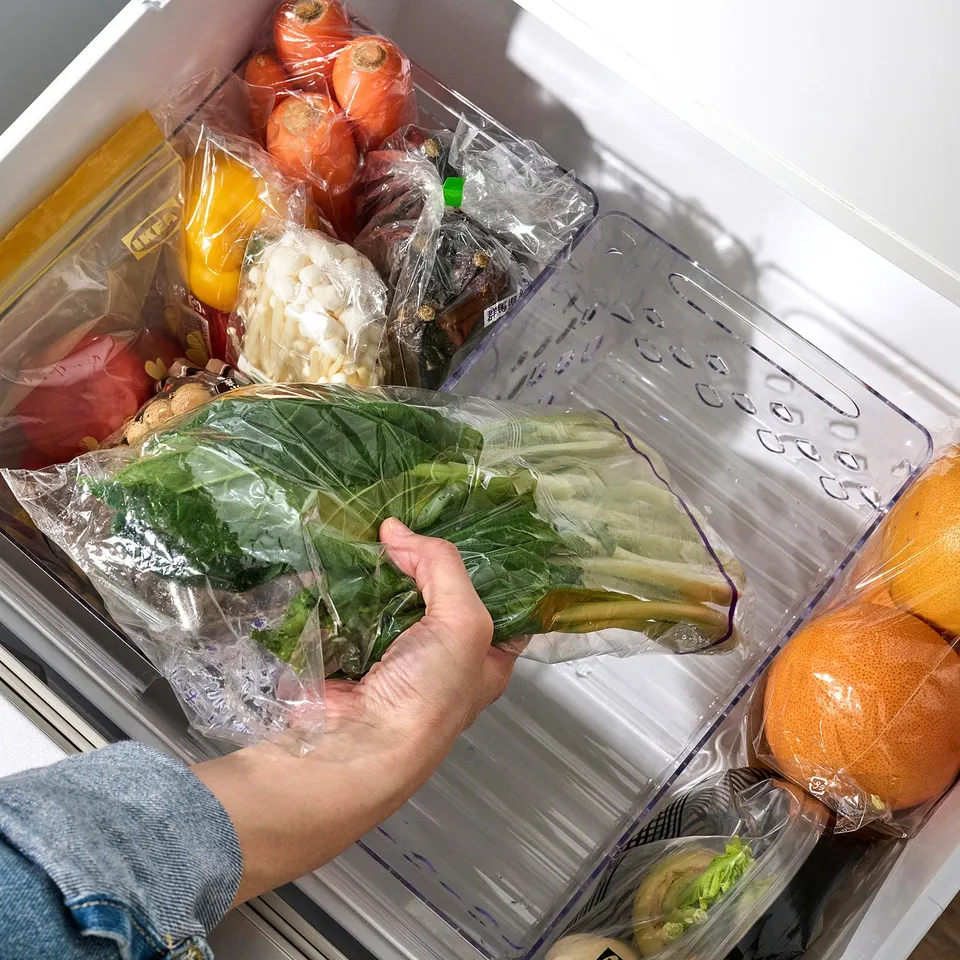 Person holding fridge basket with leafy greens, showcasing easy use and ventilation.