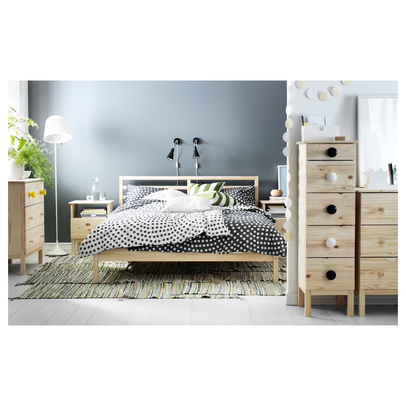 Modern bedroom featuring TARVA wooden bed with dot bedding, two wooden dressers, green accent pillows, and decorative lights.